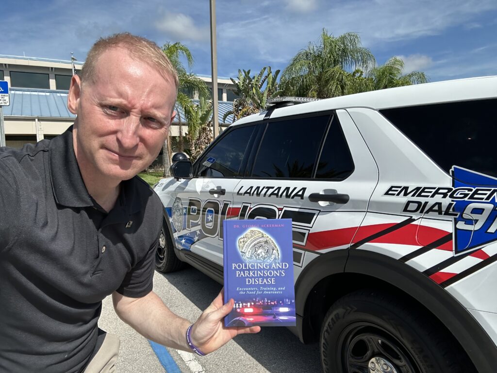 Dr. George Ackerman with a Lantana Police vehicle and the book